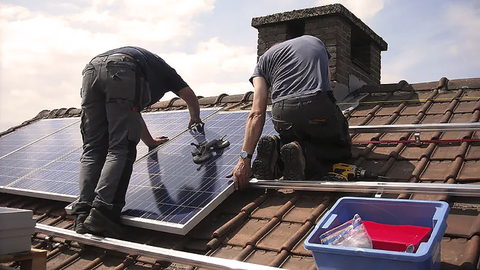 Vista de espaldas de dos hombres colocando placas solares en un tejado